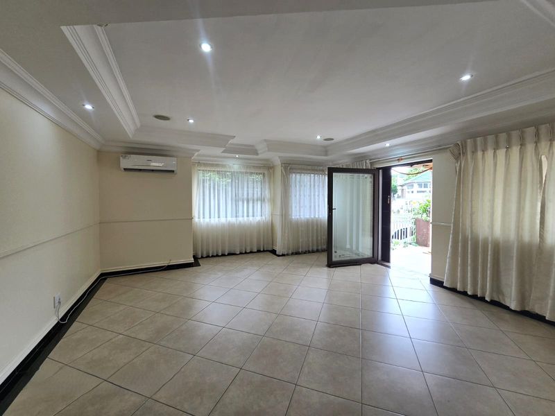 Spacious, light-filled living area featuring neutral tiled flooring, recessed ceiling with cove lighting, and a split-system air conditioner, opening directly to an outdoor space.