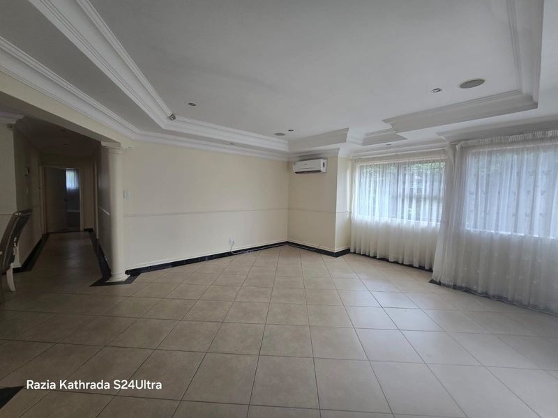 Spacious living area featuring tiled floors, recessed ceiling with crown molding, and a wall-mounted air conditioning unit.