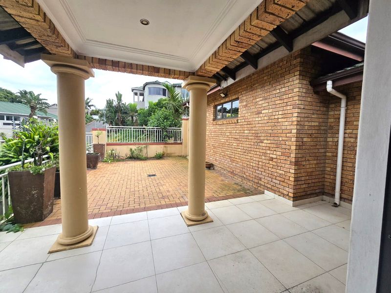 A covered patio area featuring tiled flooring, structural columns, and an adjacent brick-paved outdoor space, offering a functional area for outdoor living.
