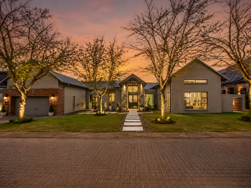 A beautifully presented modern home featuring a stone-clad entrance, brick accents, paved driveway, and well-maintained landscaping at dusk.