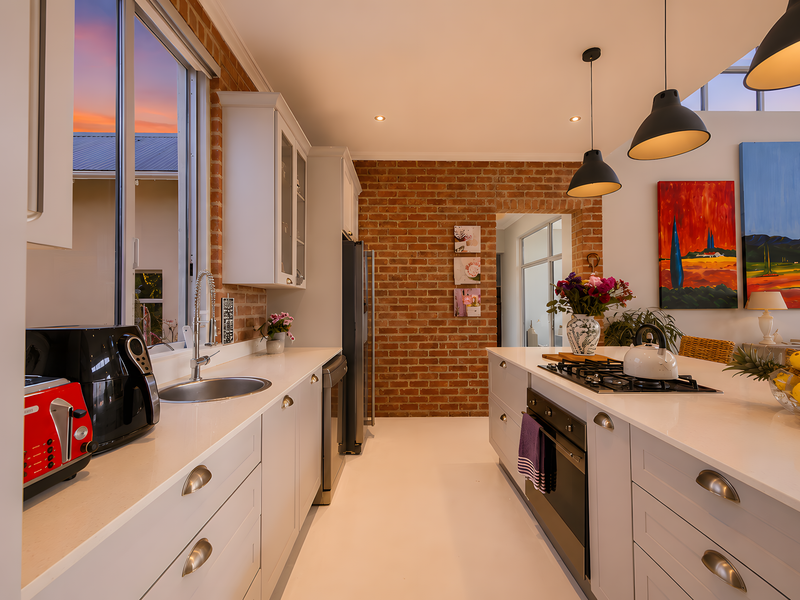 Modern kitchen featuring exposed brick walls, white shaker cabinetry, quartz countertops, a central island with gas cooktop, and integrated oven.