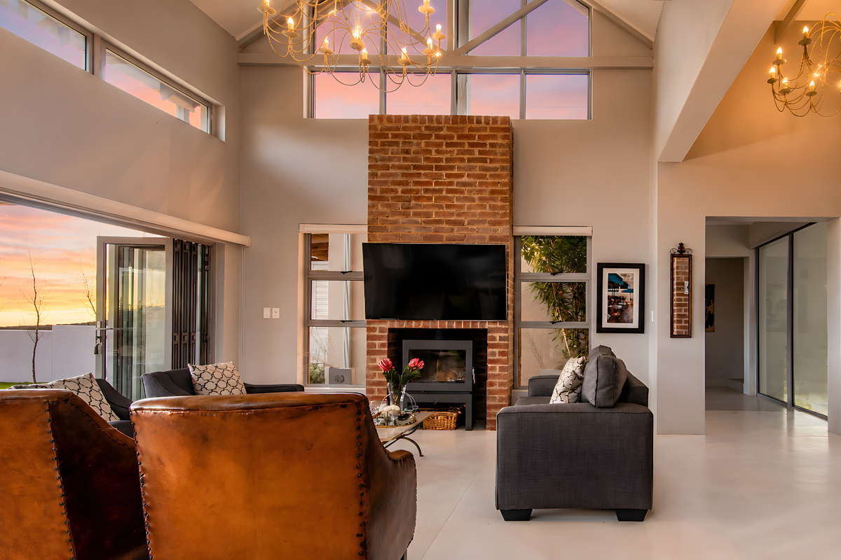 Spacious living room featuring a striking exposed brick fireplace, vaulted ceilings with timber trusses, and large bi-fold doors opening to an outdoor view.
