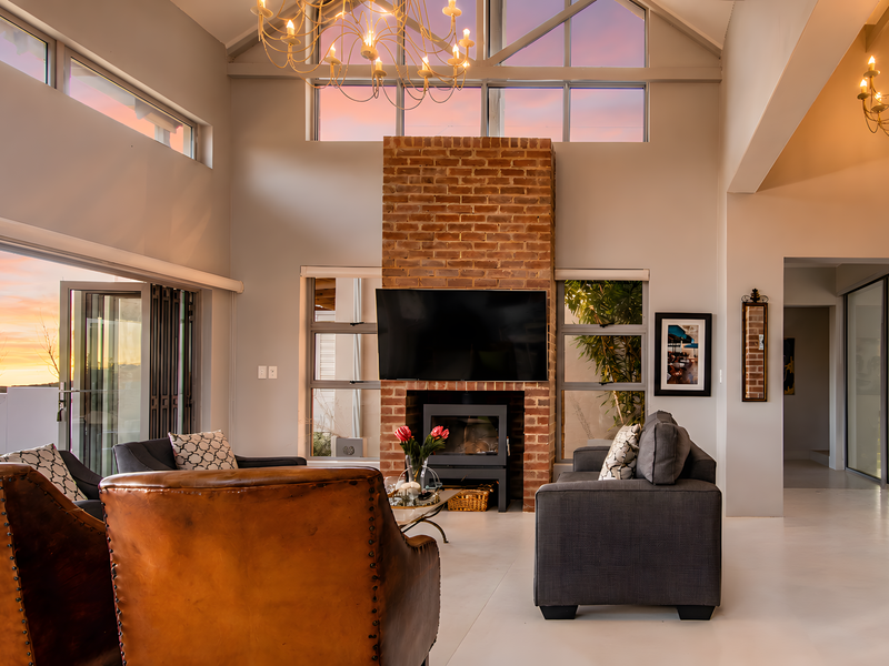Spacious living room featuring a striking exposed brick fireplace, vaulted ceilings with timber trusses, and large bi-fold doors opening to an outdoor view.