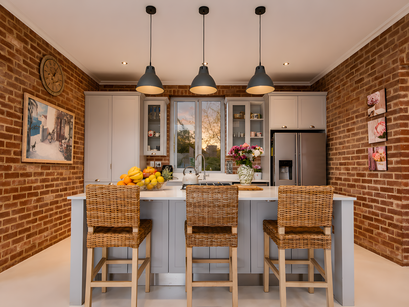 A modern kitchen featuring exposed brick walls, a central island with breakfast seating, and elegant pendant lighting, creating a warm and inviting atmosphere.