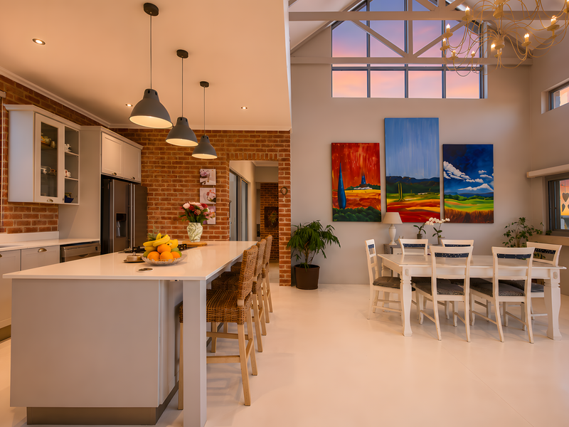 Spacious open-plan kitchen and dining area featuring exposed brick walls, a large kitchen island, vaulted ceilings, and expansive windows with sunset views.