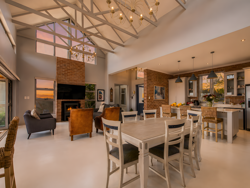 Spacious open-plan living and kitchen area featuring high vaulted ceilings with exposed trusses, a brick fireplace, and modern kitchen cabinetry with a central island.
