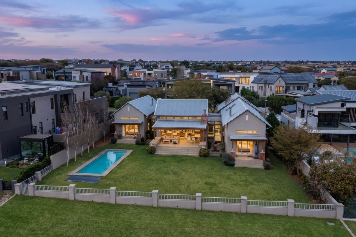 Aerial view of a modern residential property featuring a swimming pool, landscaped garden, covered patio, and metal roofing in a well-maintained estate setting.