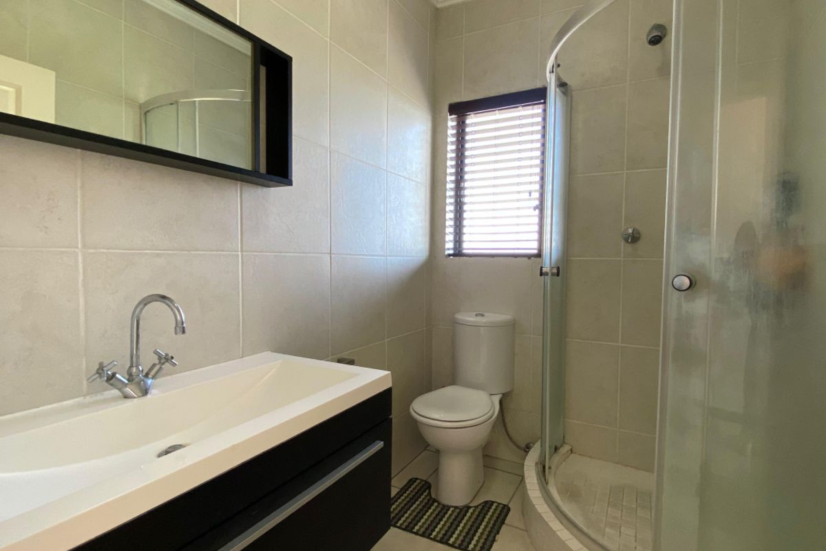 A clean, functional bathroom featuring a modern vanity, a curved glass shower enclosure, and neutral wall tiling.