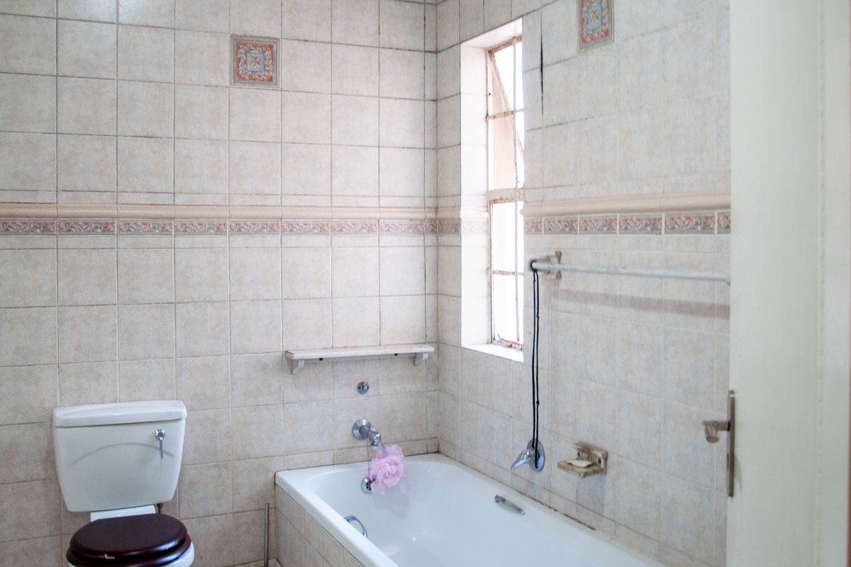 A dated bathroom featuring a standard bathtub, toilet, and tiled walls with a window providing natural light.