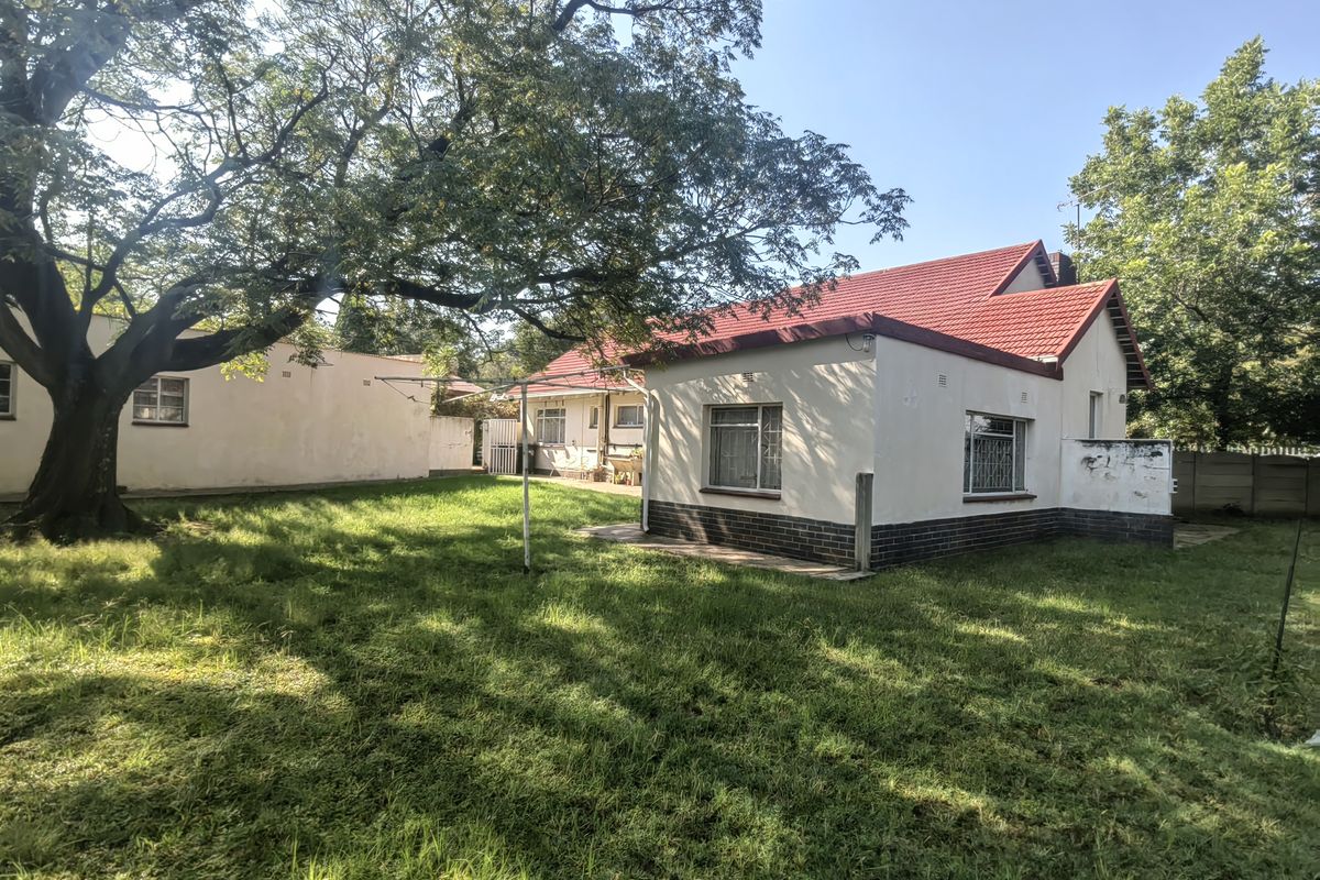 Rear view of the property featuring a red tiled roof, brick base detailing, and a spacious garden area with mature trees.