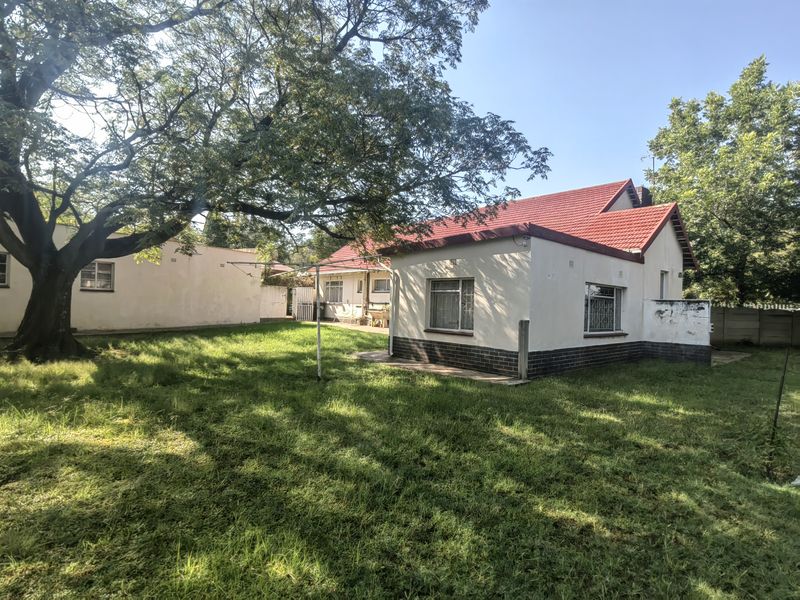 Rear view of the property featuring a red tiled roof, brick base detailing, and a spacious garden area with mature trees.