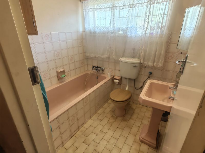 A dated bathroom featuring original pink sanitaryware, including a bathtub and pedestal basin, with tiled walls and flooring throughout.