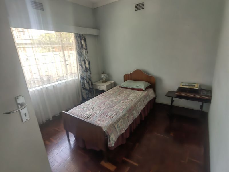 A bedroom featuring dark parquet flooring, a large window with security bars, and a ceiling air vent.