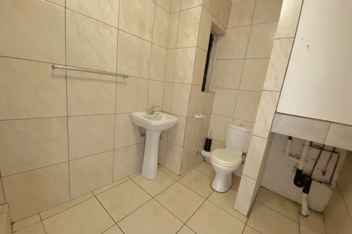 A functional bathroom featuring a pedestal sink, toilet, and floor-to-ceiling wall tiling, requiring some finishing work around the exposed plumbing area.
