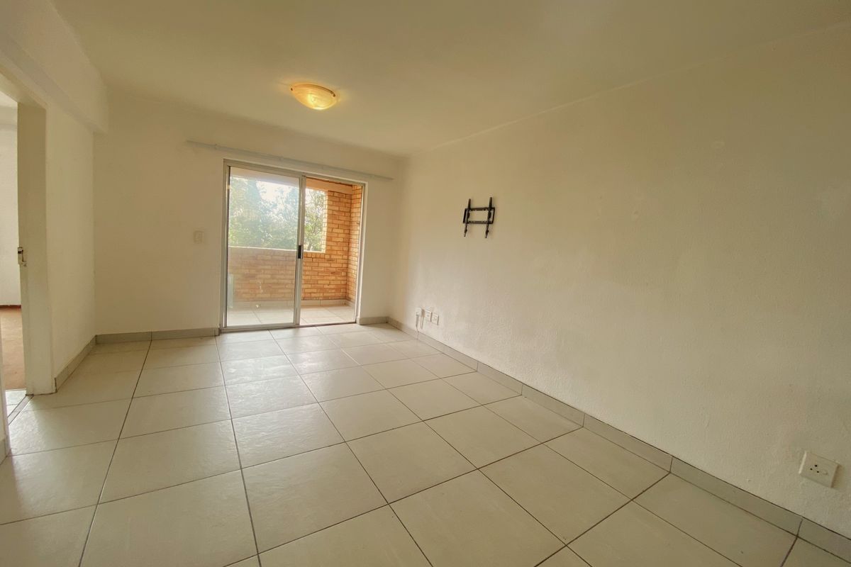 An empty living room featuring neutral floor tiles, a ceiling light fixture, and a sliding glass door leading to a brick-walled balcony.
