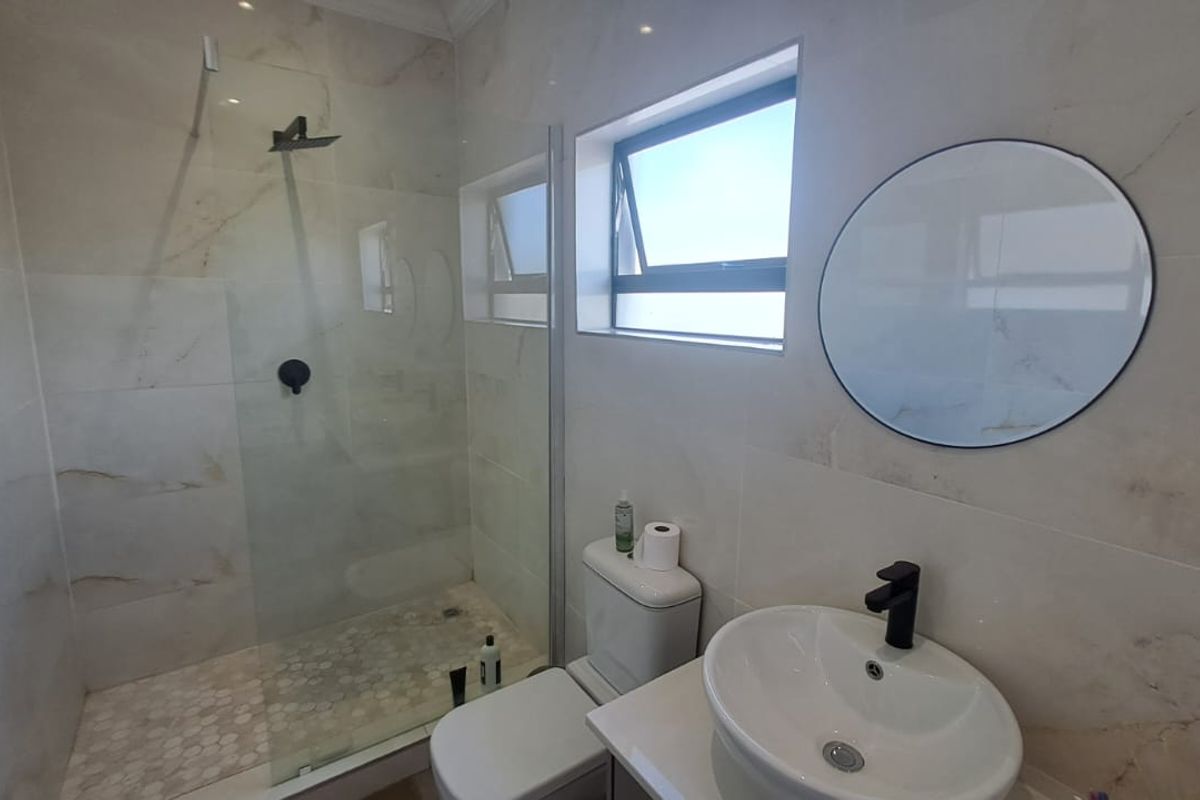 Modern bathroom featuring a walk-in shower with glass screen, black fixtures, and contemporary vanity basin with marble-look wall tiling.