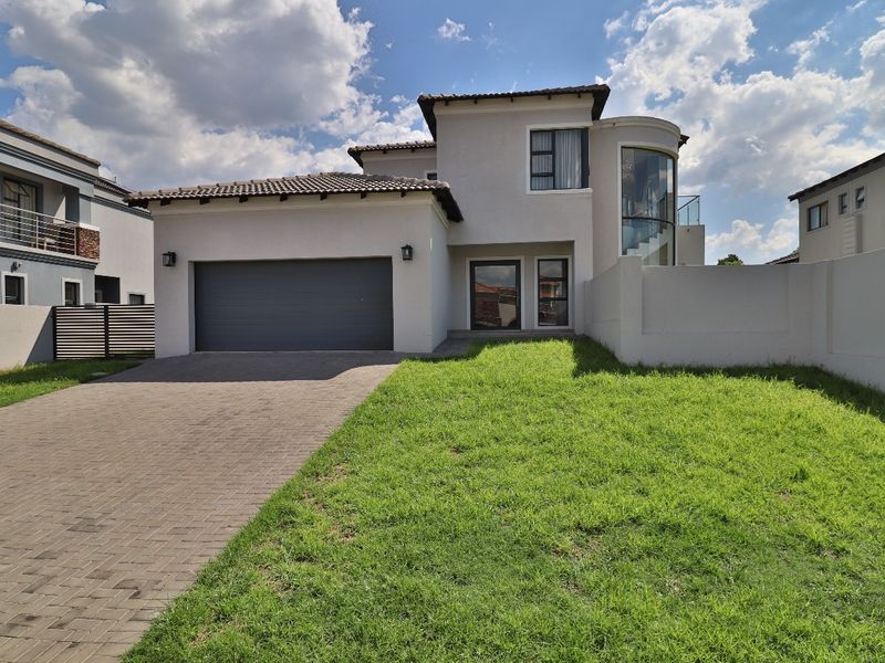Modern double-story residential home featuring a paved driveway, double garage, and a distinctive curved glass architectural element.