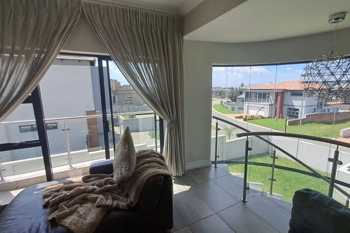 Bright living area featuring large format floor tiles, a curved glass balustrade, and expansive windows offering elevated views of the surrounding neighbourhood.