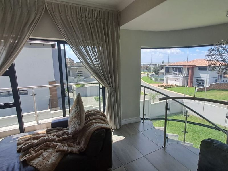 Bright living area featuring large format floor tiles, a curved glass balustrade, and expansive windows offering elevated views of the surrounding neighbourhood.