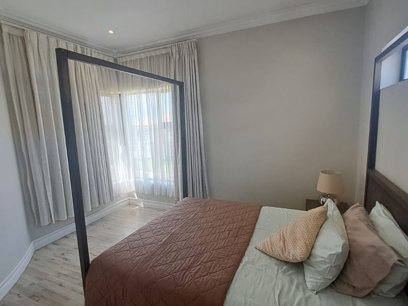 A well-lit bedroom featuring a bay window, neutral wall finishes, coving, and light-toned laminate flooring.