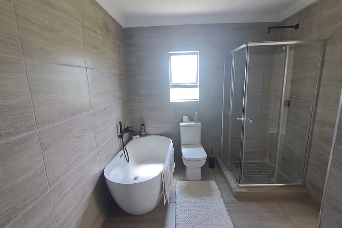 Modern bathroom featuring a freestanding bathtub, a separate glass-enclosed shower, and neutral floor-to-ceiling tiling.