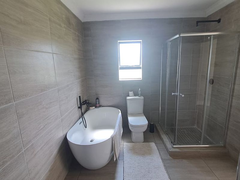 Modern bathroom featuring a freestanding bathtub, a separate glass-enclosed shower, and neutral floor-to-ceiling tiling.
