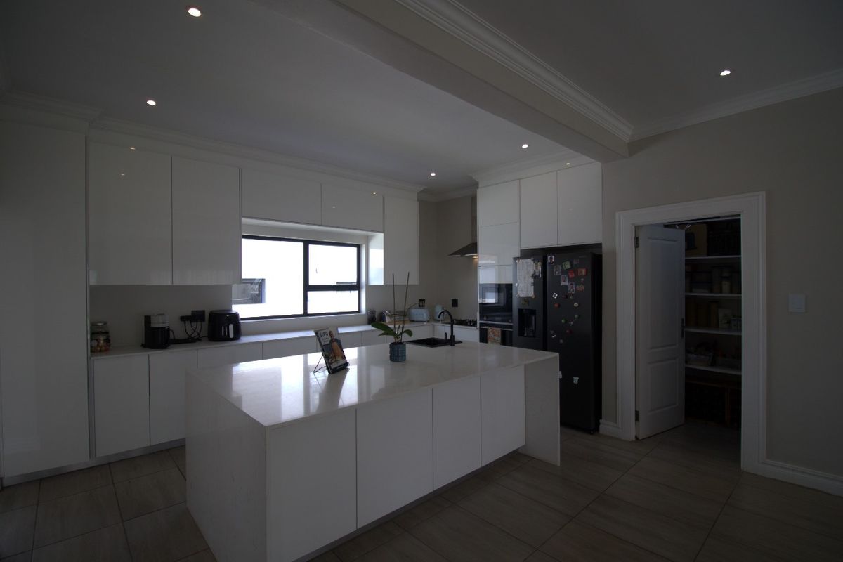 Modern kitchen featuring white cabinetry, a central island with quartz countertops, recessed lighting, and an adjacent walk-in pantry.