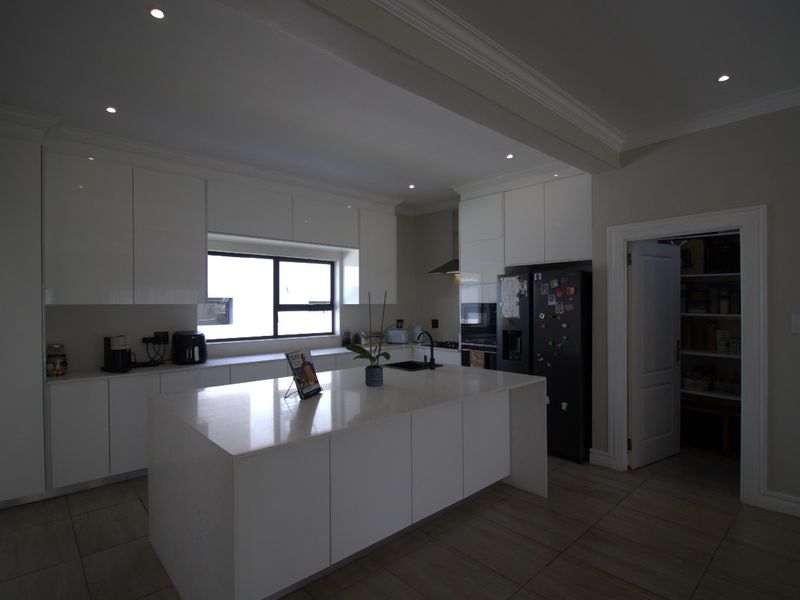Modern kitchen featuring white cabinetry, a central island with quartz countertops, recessed lighting, and an adjacent walk-in pantry.