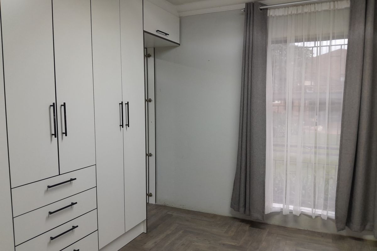 A bright bedroom featuring modern white built-in cupboards with black hardware and stylish herringbone flooring.