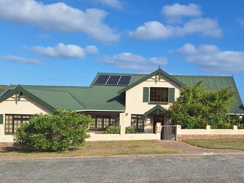 Front elevation of a well-maintained house featuring a green corrugated metal roof, solar panels, and a paved entrance walkway with a boundary wall.