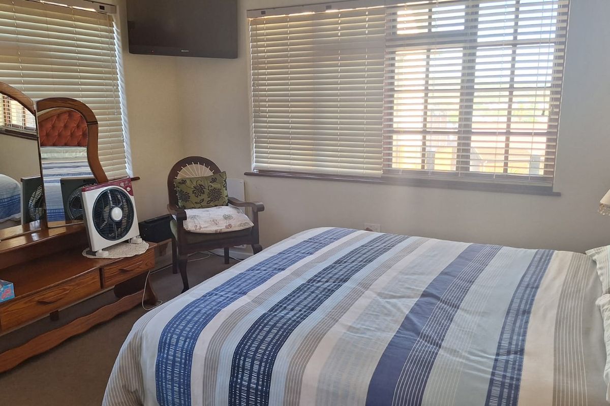 A functional bedroom featuring neutral walls, carpeted flooring, and venetian blinds on the windows.