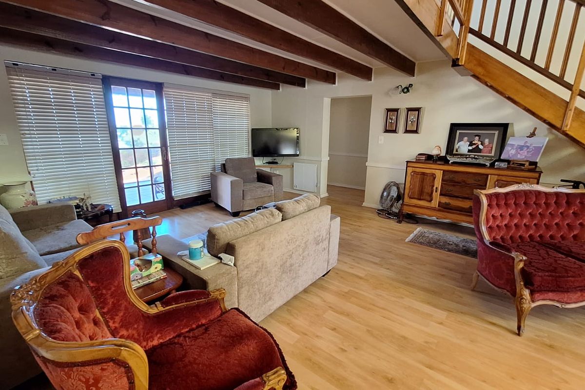 Spacious living room featuring exposed timber ceiling beams, laminate flooring, and a wooden staircase, with direct access to the outdoor area through a french door.