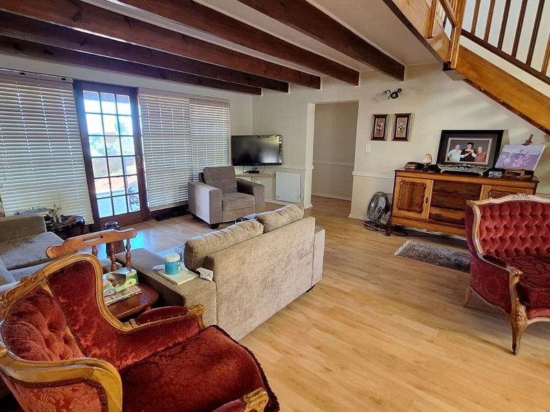 Spacious living room featuring exposed timber ceiling beams, laminate flooring, and a wooden staircase, with direct access to the outdoor area through a french door.