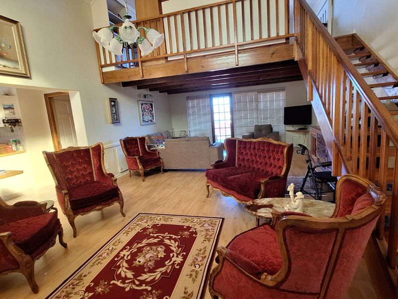 Spacious open-plan living area featuring a wooden staircase, mezzanine level, exposed timber beams, and integrated kitchen cabinetry with laminate flooring.