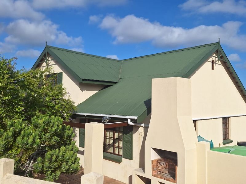 Rear elevation of a house featuring a green corrugated metal roof, built-in outdoor fireplace, and timber window shutters.