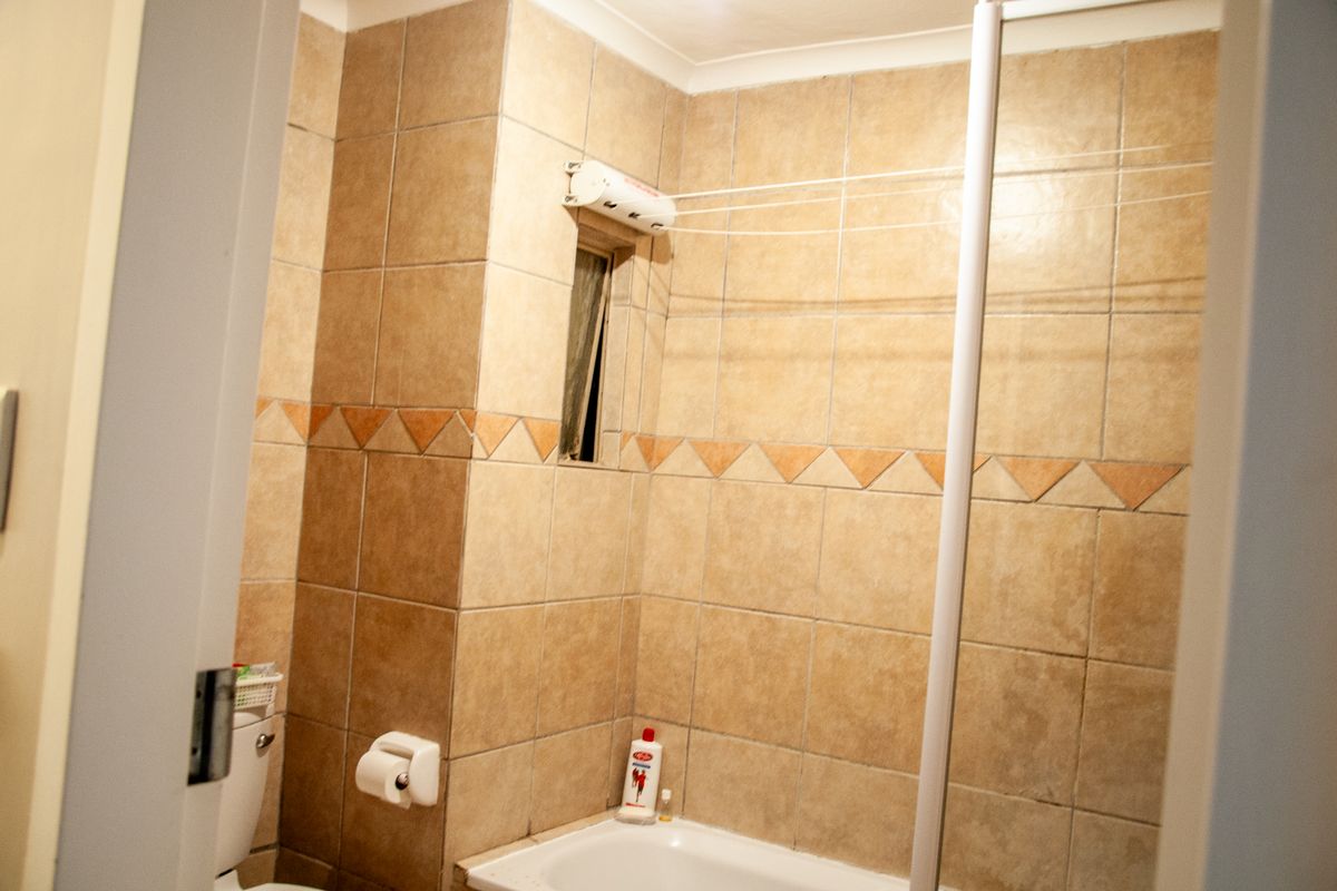 A functional bathroom featuring full-height wall tiling, a built-in bathtub, and a wall-mounted retractable clothes drying line.