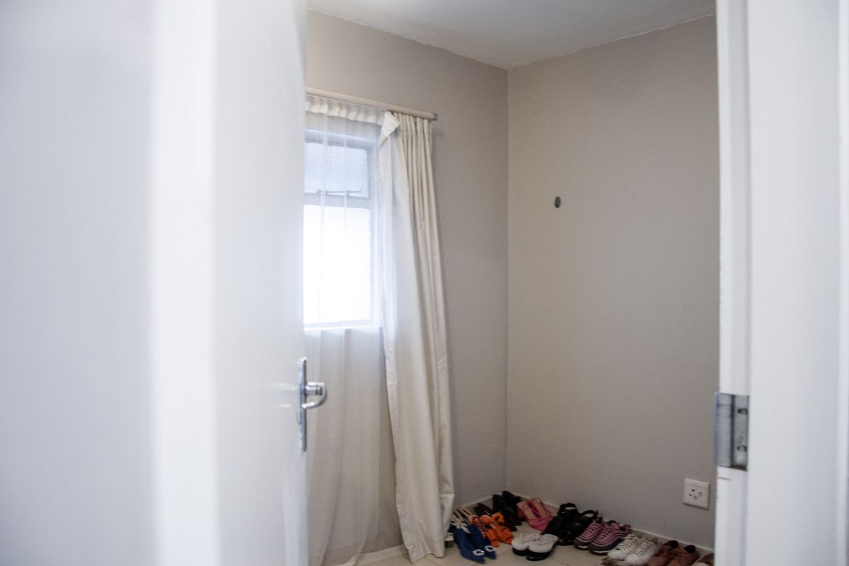 A compact bedroom or utility space featuring neutral wall tones, a window with curtain track, and electrical power points.