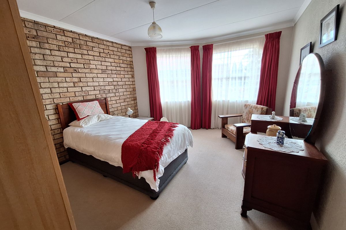 A bedroom featuring a distinctive exposed brick feature wall, neutral carpeting, and large windows that provide ample natural light.