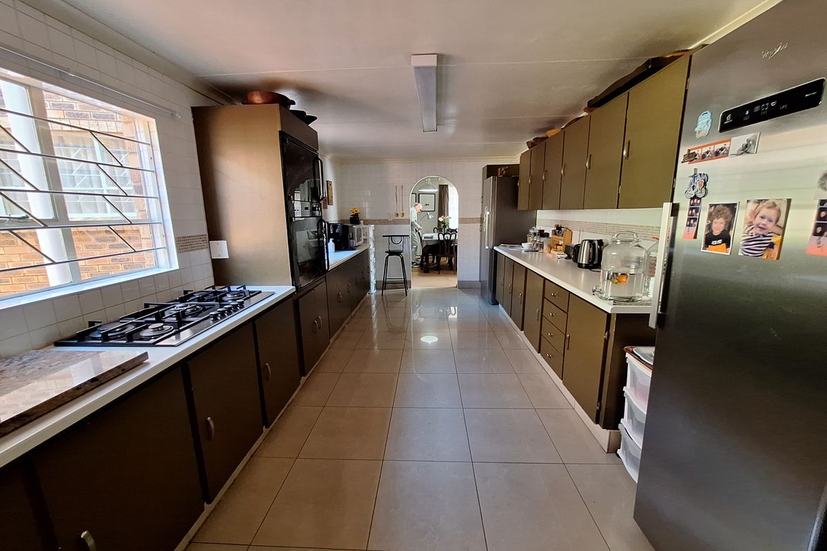 A spacious galley-style kitchen featuring tiled flooring, extensive built-in cabinetry, a gas hob, and a built-in oven, leading through an archway to the dining area.