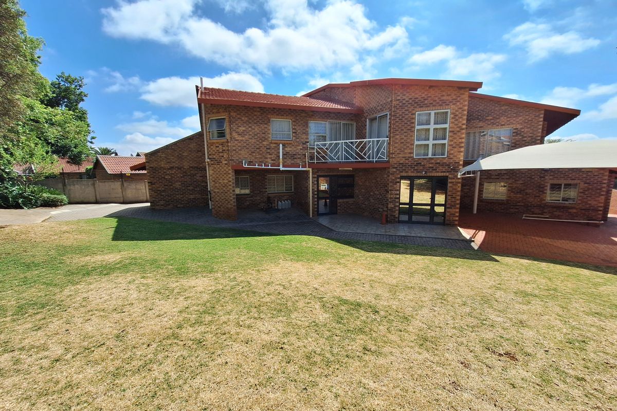 Rear view of a multi-level brick house featuring a balcony, paved patio area, and a spacious lawn.