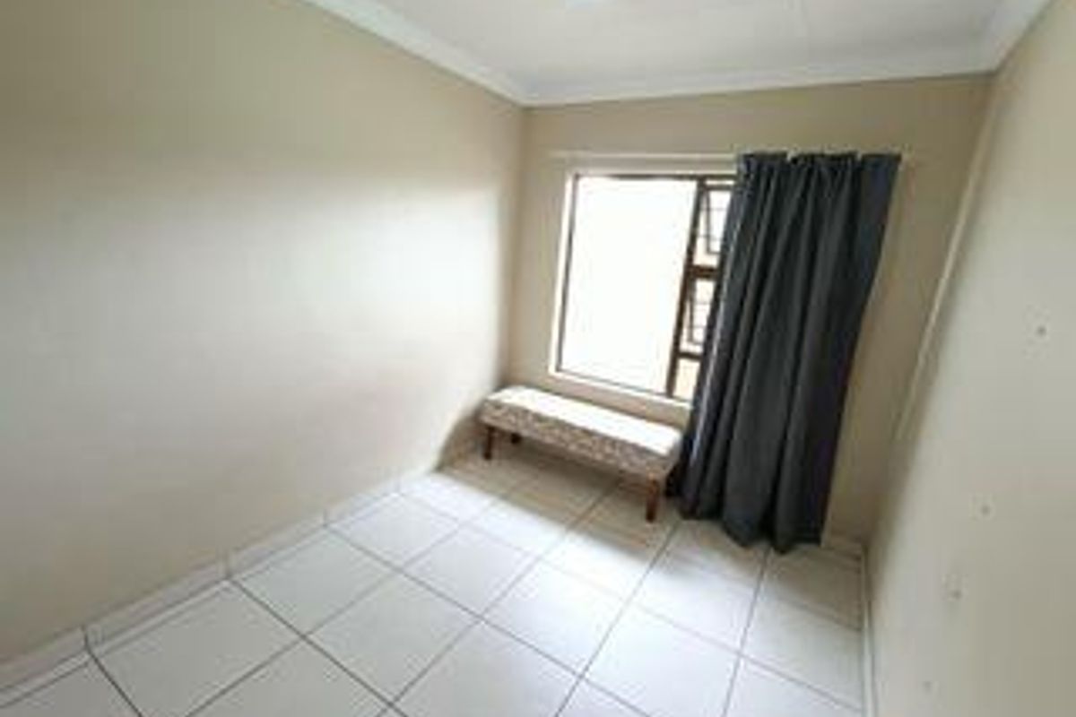 A simple, neutral-toned bedroom featuring tiled flooring and a window with security bars.