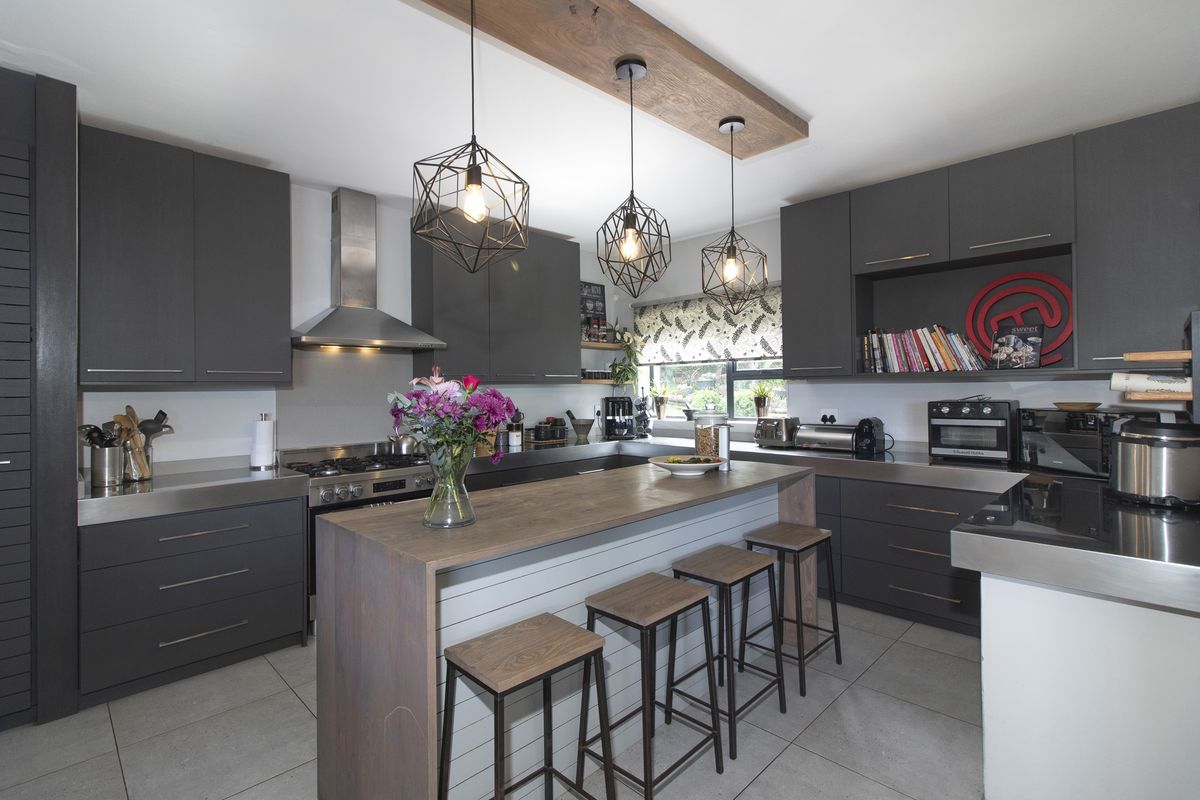 Modern kitchen featuring dark cabinetry, stainless steel countertops, a central island with seating, and high-quality finishes throughout.