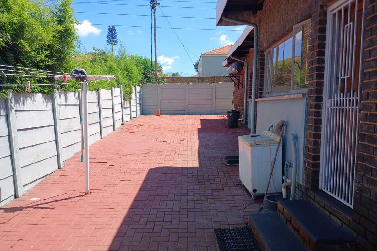 A paved rear courtyard area featuring a brick exterior wall, security gate, and perimeter walling, providing a functional outdoor utility space.
