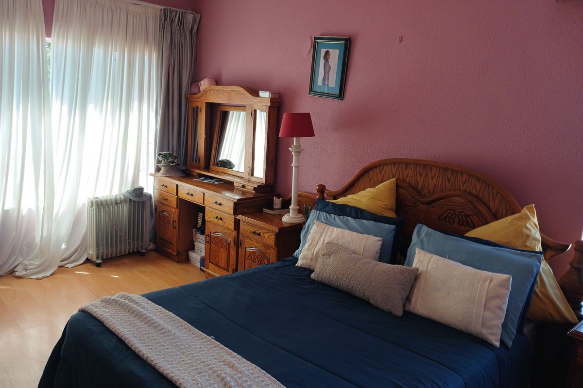 A bedroom featuring laminate flooring, large window with curtains, and a radiator.