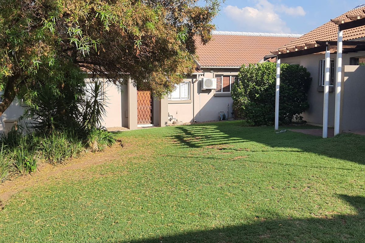 A private rear garden featuring a well-maintained lawn, a wooden pergola structure, and direct access to the apartment building.