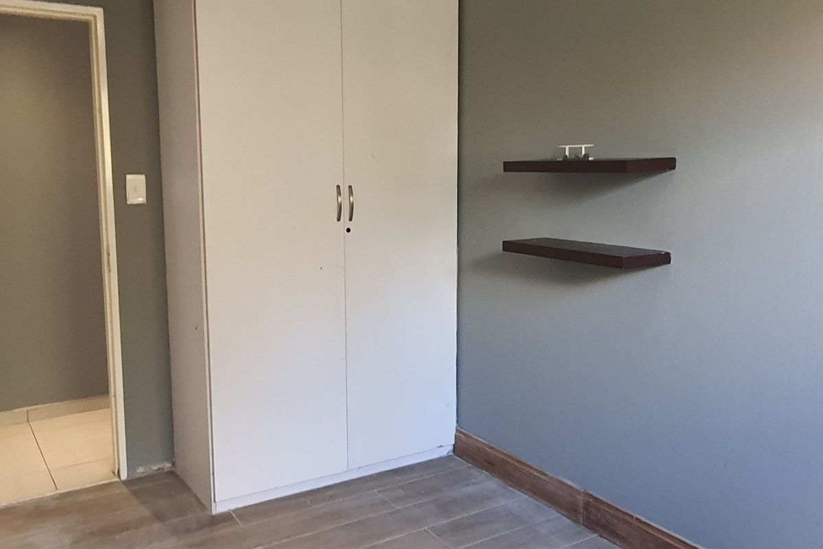 A bedroom featuring a built-in wardrobe, floating wall shelves, and tiled flooring with neutral grey wall paint.