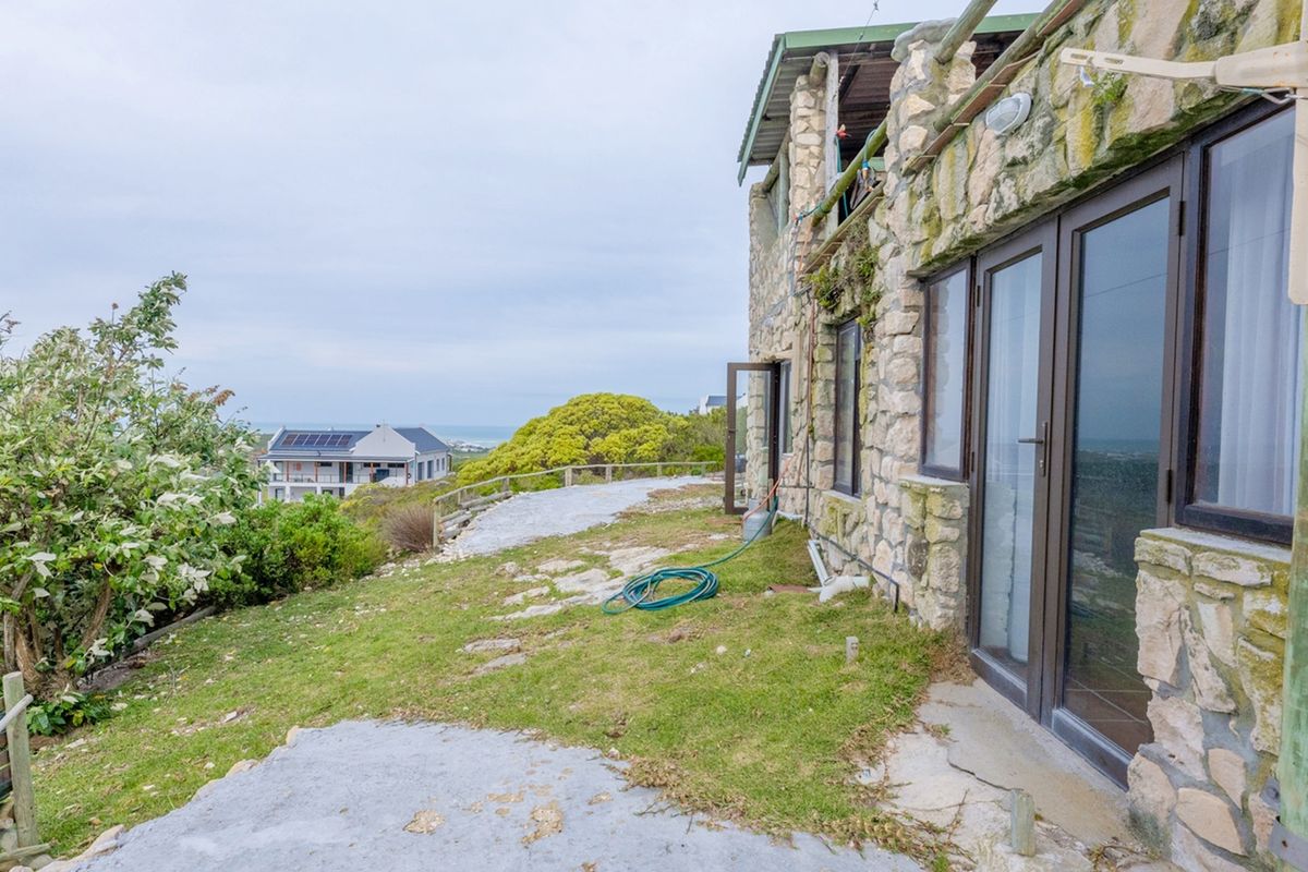 Rear exterior view of a stone-clad cottage featuring glass doors opening onto a concrete patio area with coastal views.