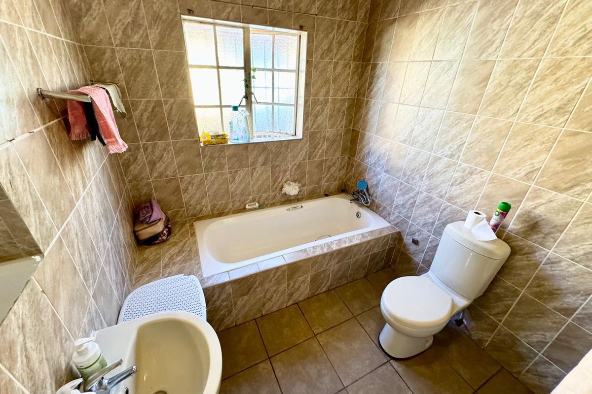 A functional bathroom featuring a built-in bathtub, pedestal basin, and toilet, finished with full-height wall tiling and a window for natural light.