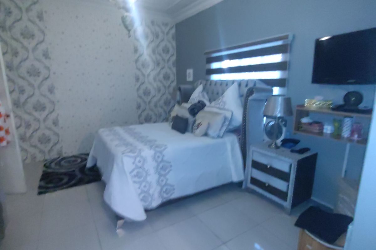 A bedroom featuring tiled flooring, decorative wallpaper accents, and fitted roller blinds.