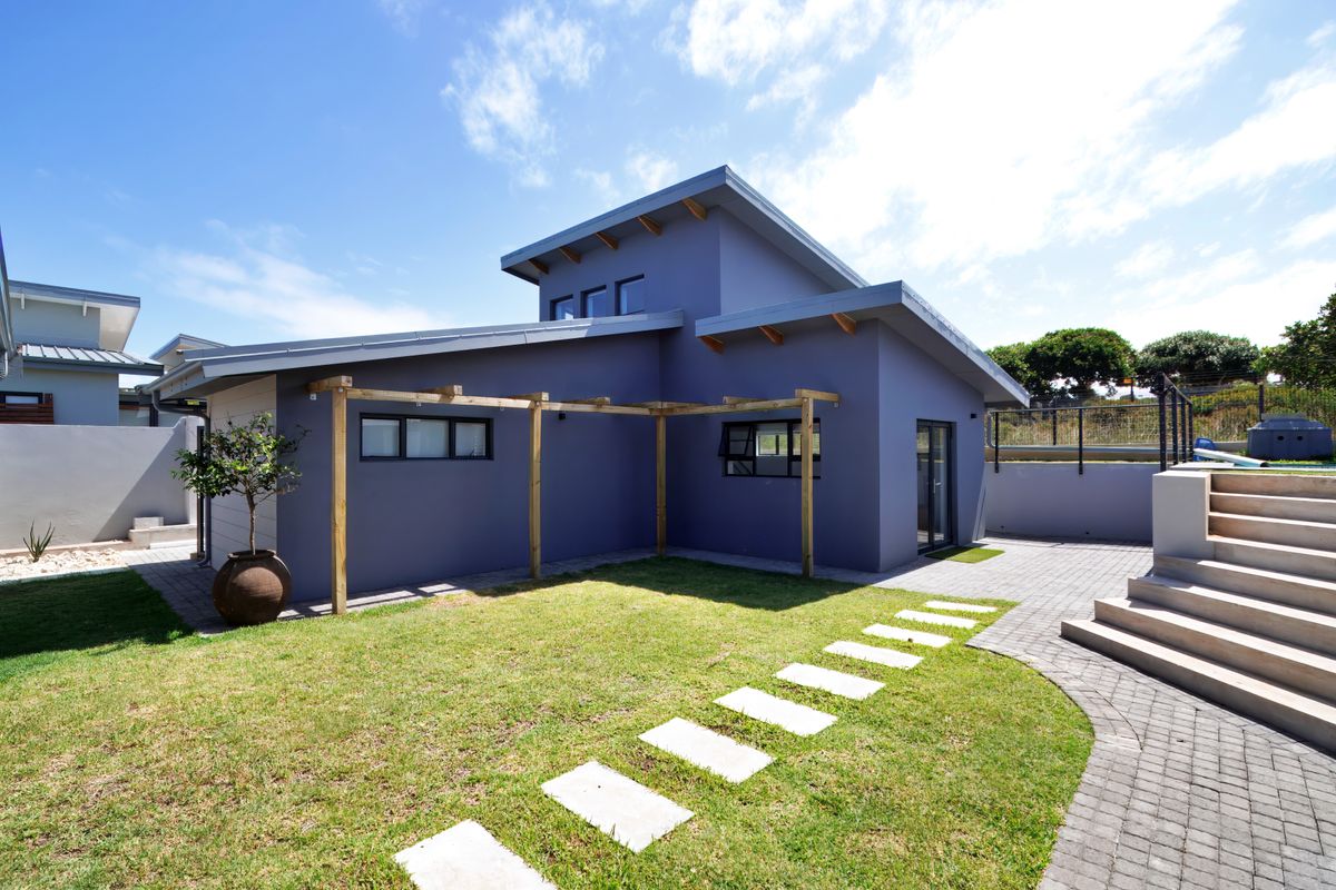 Rear view of a modern home featuring a timber pergola, paved pathways, concrete stairs, and a well-maintained lawn area.